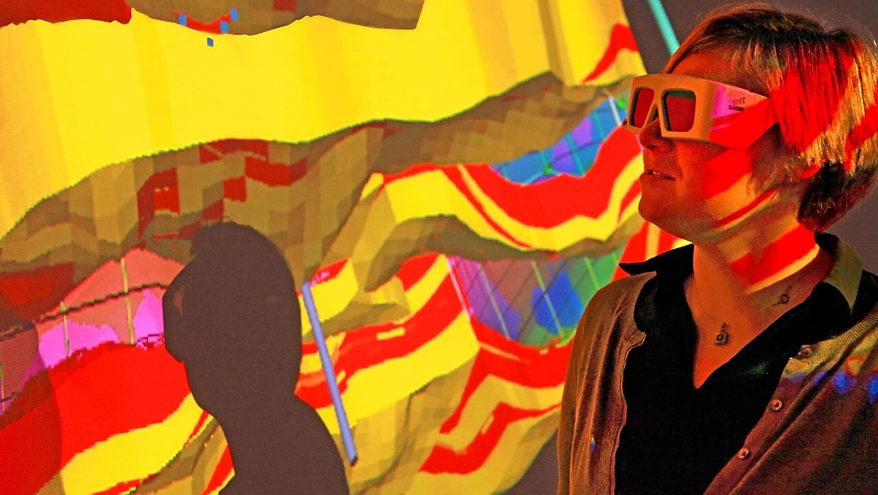 Una mujer con gafas especiales examina una proyección en 3D de un mapa geológico